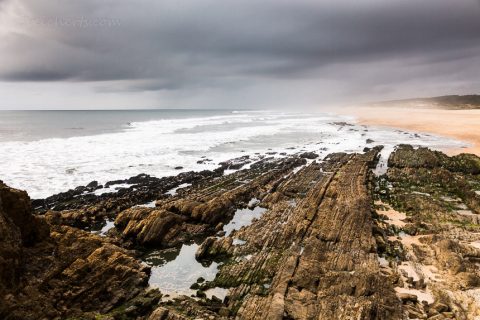 Regen kommt auf, die Felsen am Strand beherbergen interessante Gezeitenbecken